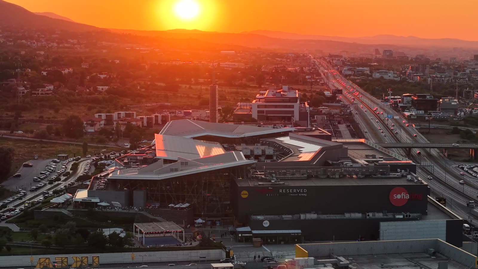 Sofia Ring Mall от птичи поглед по залез — слънцето над планината и светлините на София зад мола